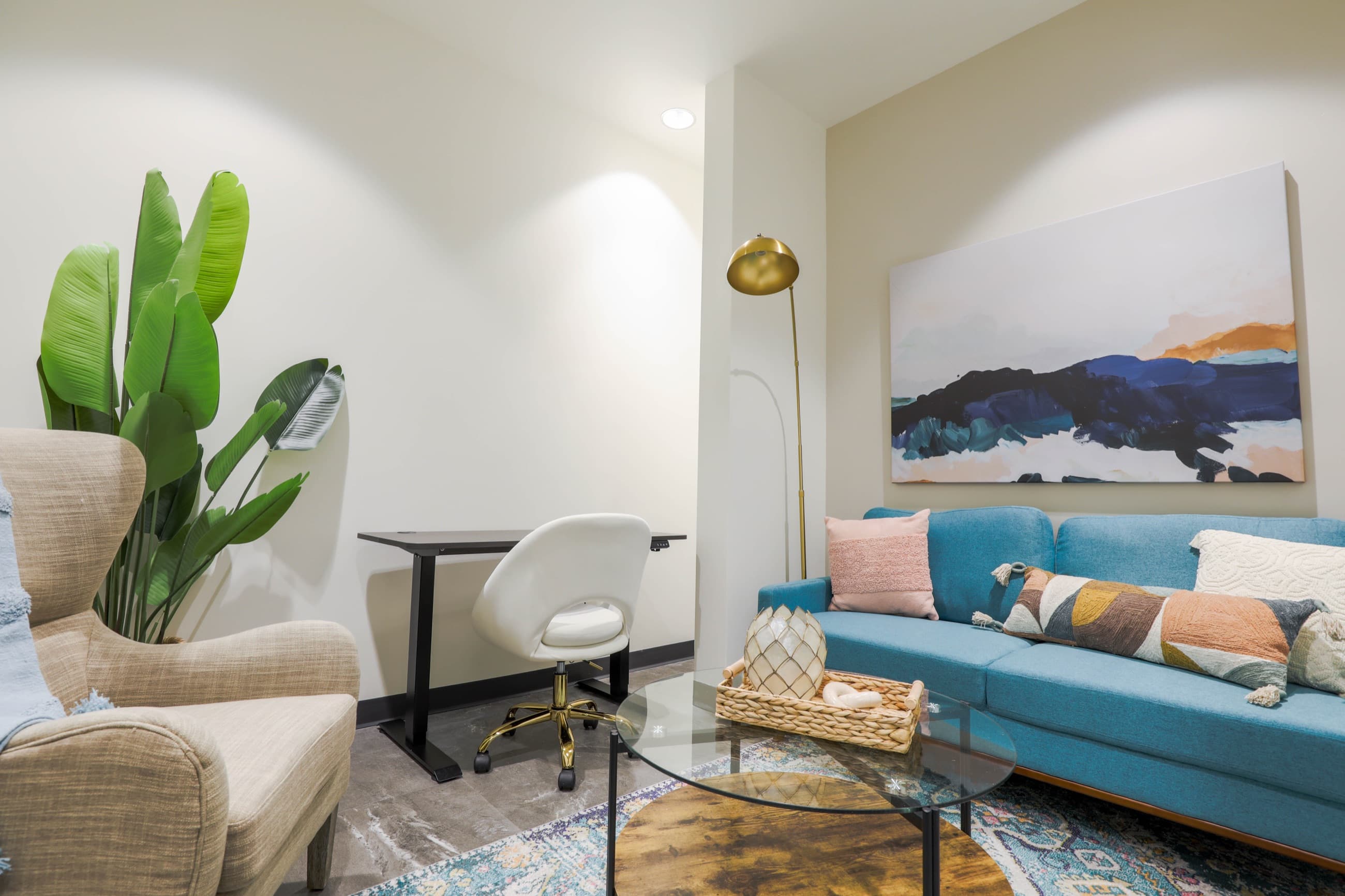 Suite with a teal sofa, woven armchair, plant and gold floor lamp